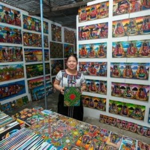 Woman holds artwork in front of wall filled with paintings.
